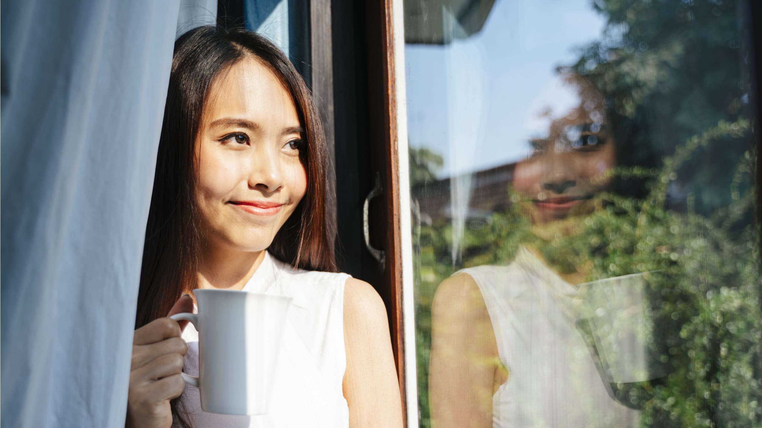 Woman enjoys a cup of tea while looking out a window.
